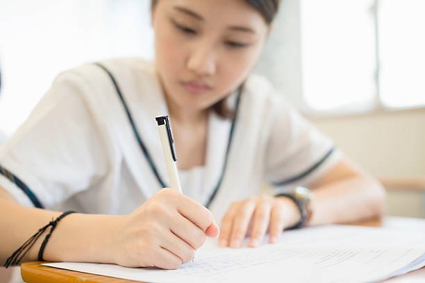 Female student writing Chinese Language exam, HK, Asia.